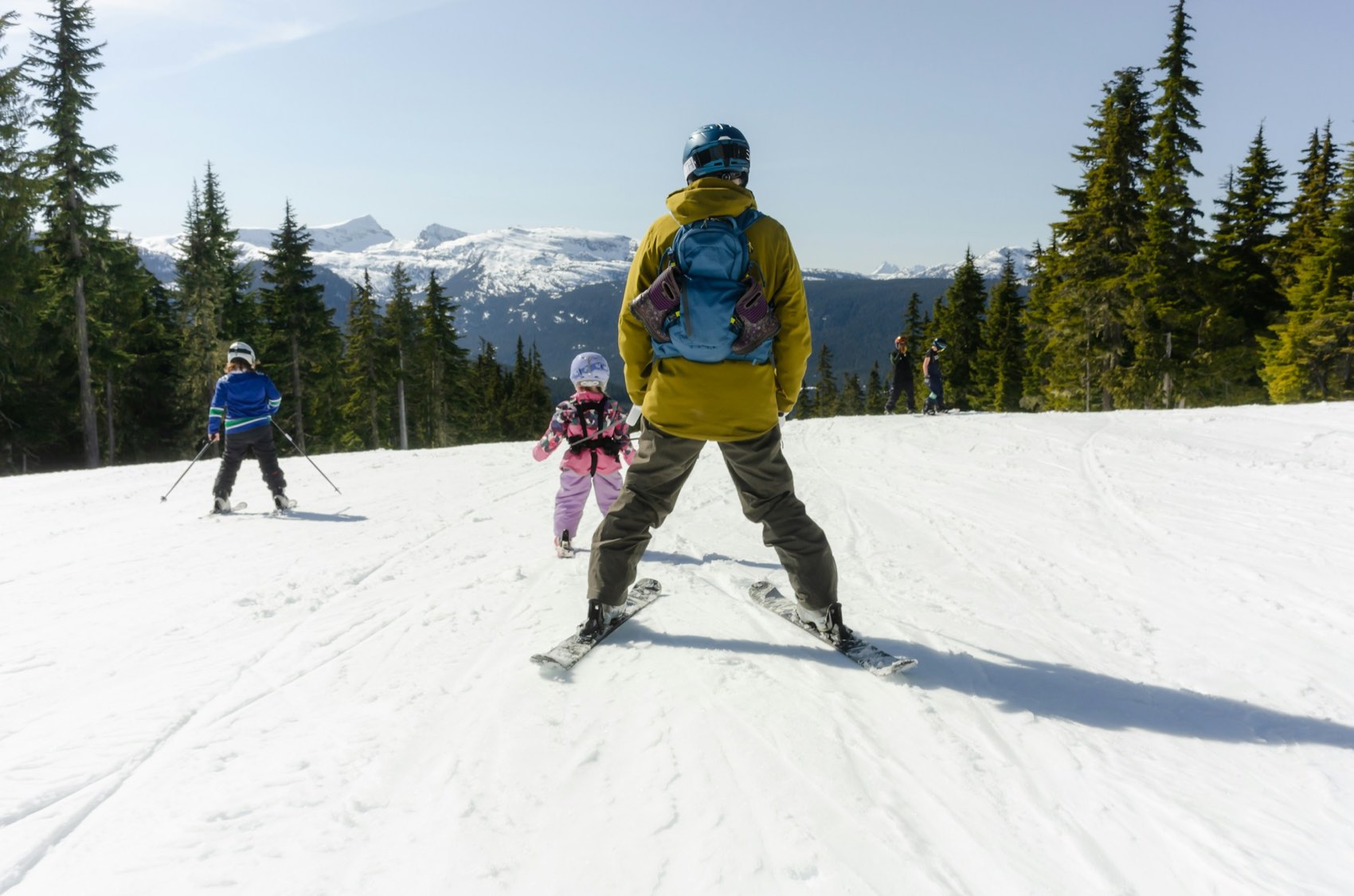 Three skiers descending a snowy slope together with forested ridges behind